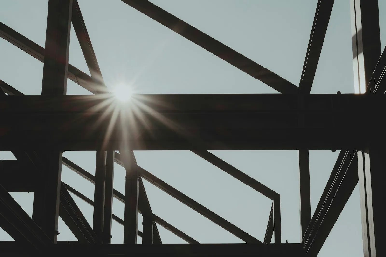 Ein stählernes Traggerüst im Gegenlicht, die Sonne bricht zwischen den Streben hindurch.
